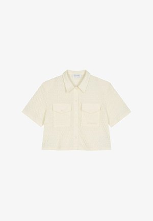 Majica s kratkimi rokavi, skrajšana v off-white teksturiranem materialu, ki ima gumbasto zapiranje spredaj in dve žepki na prsih.