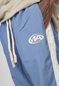 Ljusblå shorts i lättviktsmaterial, med en vit sido panel och en synlig logotyp. Midjebandet har beige dragsnöre.
