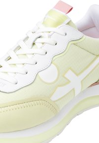 Baskets de sport vert clair et blanches avec un dessus texturé, un design festonné, un système de laçage blanc et un accent de talon rose.