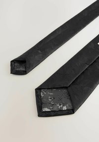Fekete nyakkendő finom levélmintával, texturált anyagból készült; a hegyénél fényes ezüst virágmintás bélés található.