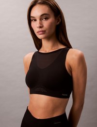 Črn športni modrček z zaobljenim izrezom, prosojnimi paneli in perforiranimi detajli na dnu. Vsebuje blagovno znamko Calvin Klein.