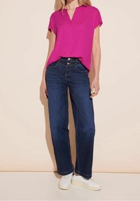 Kort rosa topp med v-ringning och korta ärmar, i kombination med mörkblå raka jeans och vita sneakers. Slät tyg, avslappnad design.