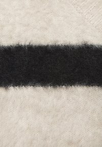 Pletená textília s jemným bielym a béžovým podkladom a výraznou čiernou huňatou horizontálnou prúžkou uprostred.