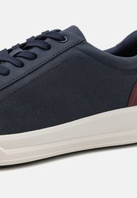 Tengerészeti vászon sportcipő,Textúrázott felsőrésszel, lapos szőtt pántokkal és kontrasztos bordó díszítéssel a sarkán. Fehér gumitalp diszkrét mintázattal.