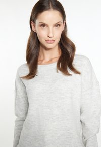 Pulover gri deschis cu o textură moale, având un decolteu larg și umeri căzuți. Materialul pare confortabil și ușor melanjat.