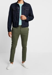 Ciemna kurtka z denimu, niebiesko-biała koszulka w paski, oliwkowe spodnie i białe wsuwane buty. Casualowy strój o luźnym kroju.