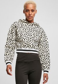 Strihnutá mikina v béžovej farbe s čiernym leopardím vzorom, s kapucňou na šnúrku a pruhovanými manžetami, skombinovaná s čiernymi legínami.