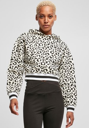 Bežinė trumpa džemperė su juodu leopardų raštu, su juosta ant kapšo ir dryžuotais rankogaliais, derinami su juodomis legginsais.