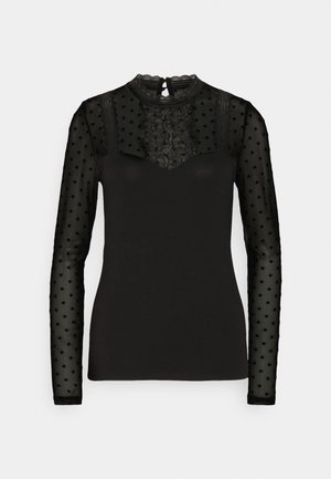 Black top featuring long sheer polka dot sleeves, a lace panel at the chest, and a rounded neckline with a back keyhole closure.