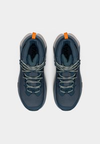 Ζευγάρι σκούρα μπλε παπούτσια πεζοπορίας με γκρι σόλες και πορτοκαλί θηλιές στη φτέρνα, σε λευκό φόντο, από πάνω.