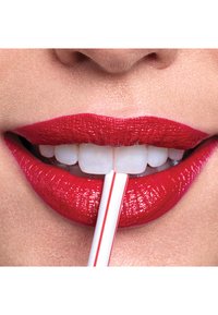 Zbliżenie na żywe czerwone usta z błyszczącym wykończeniem, trzymające słomkę. Białe zęby są widoczne między wargami, a powierzchnia jest gładka i teksturowana.