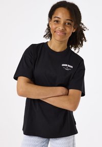 Camiseta de algodón negra con mangas cortas, un escote redondo y un gráfico de texto en blanco que dice "BUENOS DÍAS" en el lado izquierdo del pecho.