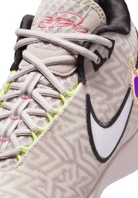Scarpa sportiva con tessuto beige chiaro a motivo, logo swoosh bianco, dettagli di lacing giallo neon e firma ricamata rosa sulla linguetta.