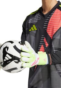 Gants de gardien de but avec des accents blancs et vert néon, des paumes texturées et un poignet ajusté, tenant un ballon de soccer noir et blanc à motifs.