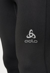 Leggins atléticos negros hechos de material elástico, con un logo plateado de Odlo y costuras planas para mayor comodidad y durabilidad.