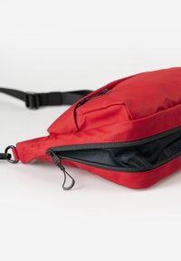 Rote, stoffliche Umhängetasche mit glatter Textur, ausgestattet mit einer Reißverschlusstasche und einem schwarzen Innenfutter. Mit verstellbarem Tragegurt und minimalistischem Design.