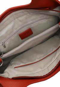 Interior de un bolso de cuero rojo con un forro suave color crema, que cuenta con un bolsillo con cremallera y dos compartimentos adicionales para la organización.