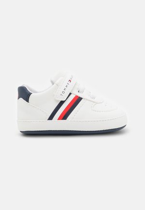 Zapatilla blanca para niño pequeño con rayas azul marino y rojas, cierre de velcro con la etiqueta "Tommy Hilfiger" y detalles en azul marino en el talón y la suela.