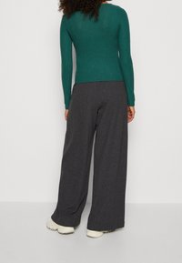 Pantalons larges gris foncé associés à un haut ajusté à manches longues en maille côtelée teal, avec un col rond et une finition tricot texturée.