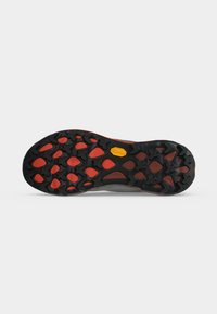 Semelle de chaussure avec une bande de roulement en caoutchouc noir et rouge présentant des motifs en forme de croix et un logo hexagonal jaune au centre.