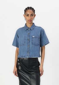 Kratka modra jeans srajca s kratkimi rokavi, zapiranje na gumb, žep na prsih in ovratnik, v kombinaciji z črno usnjeno krilo.