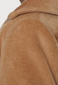 Bruine, zacht aanvoelende wollen mengseljas die een deel van de kraag en schouder toont; heeft een schone, gestructureerde vormgeving zonder versieringen.