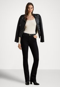 Giacca in pelle nera, top crema a coste e jeans neri svasati. Il top ha maniche lunghe e i jeans sono aderenti con cintura. Stivali neri con tacco.