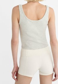 Osoba z krótkimi blond włosami, ubrana w jasnoszary top bez rękawów oraz dopasowane spodenki w kolorze białym o wysokim stanie, pokazana od tyłu.