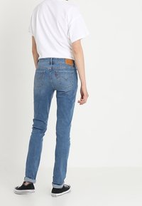 Jeans de mezclilla azul claro con corte recto, cinco bolsillos y parche de cuero en la parte posterior. Piernas ajustadas y puños enrollados.