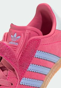 Sapatilha de camurça rosa com tecido texturizado, riscas azul claro, sola de borracha e colarinho almofadado com detalhe de logotipo em relevo.