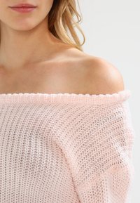 Maglione a maglia rosa chiaro con scollo a pescatore, realizzato in un tessuto morbido e testurizzato, con orli ribattuti, che mette in evidenza un design casual e arioso.