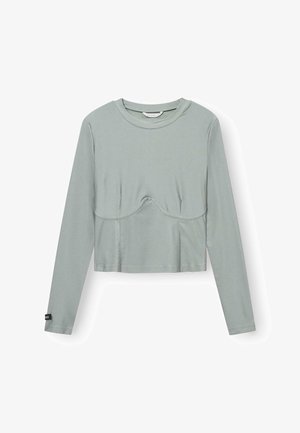 Haut cropped à manches longues en tissu vert clair avec une texture lisse. Il présente une couture centrale et un subtil détail courbé au niveau de la poitrine.