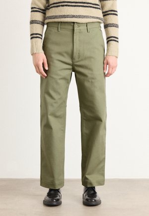 Green cotton pants with a straight-leg cut, featuring a button closure and side pockets, paired with black shoes. Textured sweater visible above.