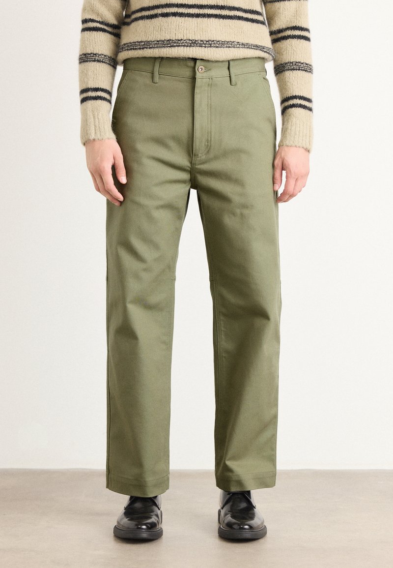 Green cotton pants with a straight-leg cut, featuring a button closure and side pockets, paired with black shoes. Textured sweater visible above.