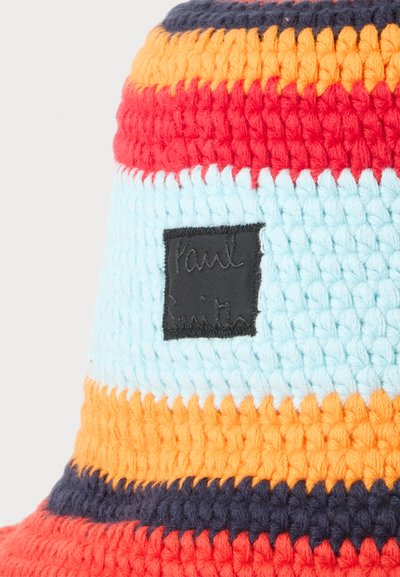 Bob multicolore en crochet avec des rayures horizontales orange, rouge, bleu clair et marine, avec une étiquette en tissu carrée noire.
