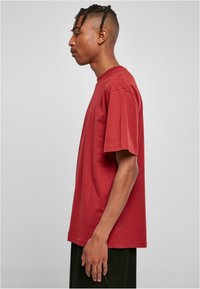 Tricou din bumbac roșu, cu mâneci scurte și guler rotund, având o croială lejeră și o textură fină, asortat cu pantaloni scurți închisi.
