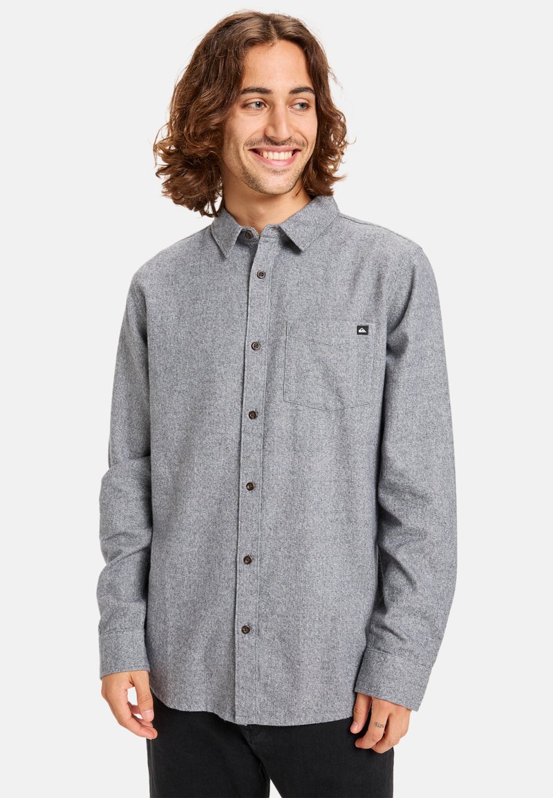 Gray flannel shirt with a button-up design, long sleeves, chest pocket, and dark buttons. Features a small logo on the pocket.