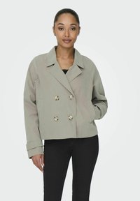Chaqueta de doble pecho en tejido gris claro, con grandes botones metálicos, un cuello y bolsillos laterales. Mangas con puños y un corte holgado.