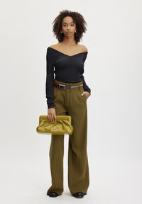 Top negru fără umeri cu textură ribbinată, pantaloni cu talie înaltă, cu carouri maro și o poșetă lucioasă de culoare verde măslinie. Pantofi negri.