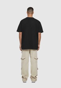 Sort bomulds T-shirt med korte ærmer, parret med beige cargo-bukser med sidelommer og en afslappet pasform. Enkel, casual design.