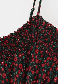 Tissu noir avec imprimé floral rouge et vert, avec un haut froncé et smocké et de fines bretelles réglables.