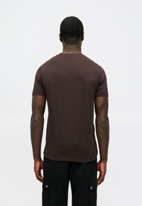 T-shirt castanho de manga curta feito de tecido suave, com um simples decote redondo e um corte reto. Usado com calças cargo pretas.