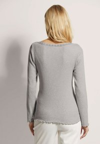 Grijze langslavige top met een geribbelde textuur, een golvende zoom en kantdetails rond de halslijn. Ontworpen voor een aansluitende silhouet.