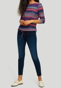 Maglione a righe multicolore con maniche a tre quarti, abbinato a jeans slim-fit blu scuro e mocassini bianchi. Il capo ha un design a maglia testurizzata.
