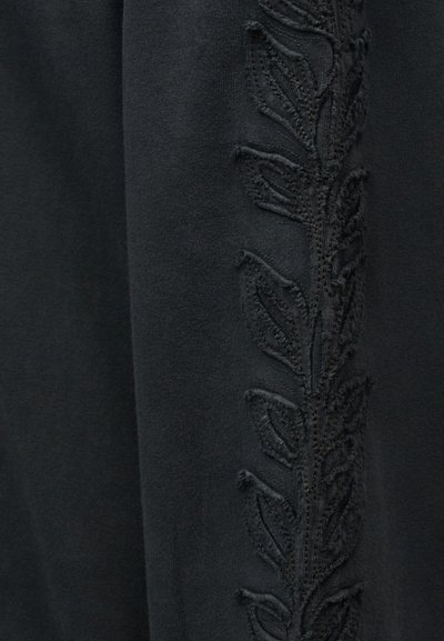 Μαύρο ύφασμα με ανάγλυφο κεντητό κάθετο σχέδιο φύλλων σε αντίστοιχο μαύρο νήμα.