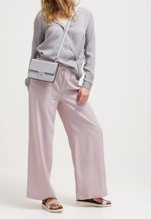 Jasnoszara, długorękawowa bluzka z dekoltem w serek, połączona z jasnoróżowymi spodniami o szerokich nogawkach. Całość uzupełniają czarne sandały z srebrnymi akcentami.