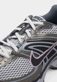 Κοντινή λήψη αθλητικού παπουτσιού Nike Air με λευκό δίχτυ, γκρι επενδύσεις, λευκά κορδόνια και μαύρο λογότυπο Nike με ροζ ραφή περιγράμματος.