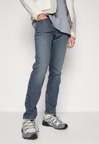 Blå denimjeans med rak passform, matchade med grå träningsskor som har ett strukturerat mönster och svarta accenter.