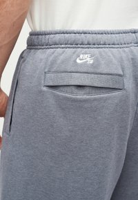 Κοντινή λήψη στη μέση ενός ατόμου που φοράει γκρι φόρμες Nike SB με ελαστική μέση και πίσω τσέπη με καπάκι.