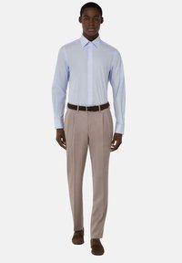 Camicia azzurro chiaro a maniche lunghe con colletto all'italiana, abbinata a pantaloni eleganti beige con pieghe e cintura e scarpe marroni.